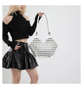 Détail d'un sac à bandoulière blanc à clous argentés porté par un mannequin femme