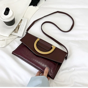 Detail of burgundy crocodile-embossed flap handbag with a large gold D-shaped buckle
