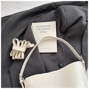 Detail of cream crocodile embossed shoulder bag on grey suit with extra strap