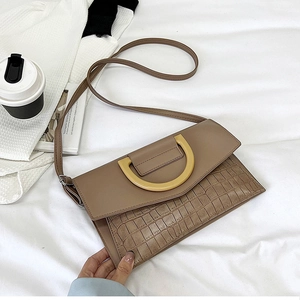 Close-up of khaki clutch bag showing crocodile texture and yellow D-ring buckle