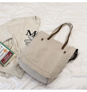 Flat lay of a beige canvas tote bag with brown straps and metal rivet detail