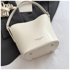 Detailed view of silver metal protective studs on the base of cream croc-embossed bucket bag