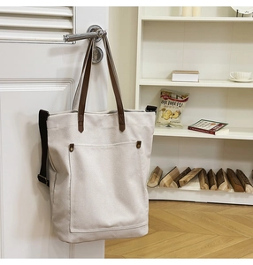 Detail of off-white canvas tote bag with dark brown leather handles and metal rivets