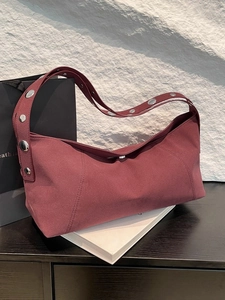 Retro burgundy suede hobo bag with silver rivets placed on a book and rock background