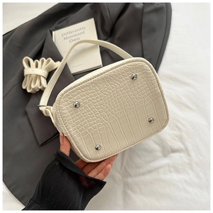 Detail shot of beige croc-embossed bucket bag showing silver bottom protective rivets