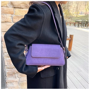Close-up of a purple matte suede underarm bag on a model wearing a black coat