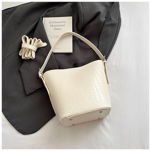 Macro detail of cream bucket bag showing crocodile texture and protective metal feet