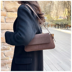 Detail of a brown suede underarm bag with a minimalist flap and metallic side hardware