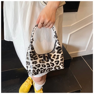 Detail of a shiny patent leather leopard print handbag held by a model in a trendy outfit