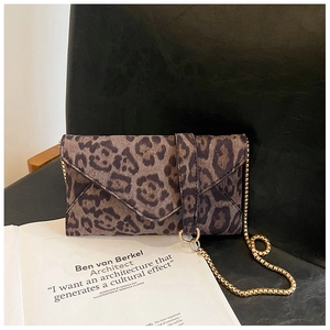 Detailed view of leopard print envelope clutch with gold metal chain on leather background