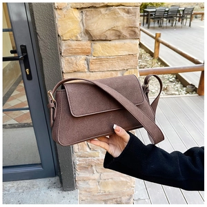 Detail of a brown matte suede shoulder bag featuring a minimalist flap and wide strap