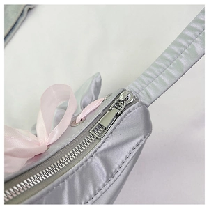 Close-up of silver satin handbag featuring a metal zipper and a pink silk bow detail