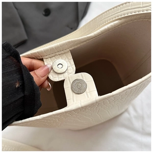 Detailed close-up of the metal magnetic clasp and crocodile pattern on the off-white bag