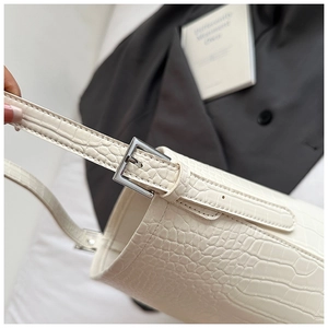 Detail of white crocodile pattern shoulder bag featuring silver metal buckle and stitching
