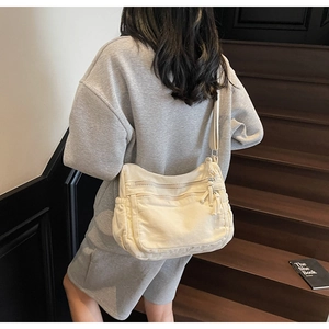 Detail view of off-white canvas crossbody bag with multiple zippers on wooden stairs