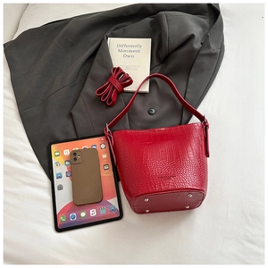 Detail view of red crocodile pattern bucket bag with bottom studs and leather texture