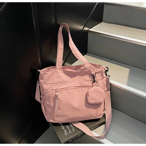 Detail view of pink nylon tote bag with small round pouch on a black book prop