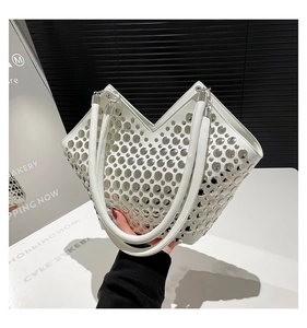 Détail d'un sac à main blanc orné de clous métalliques argentés et d'une ouverture en V