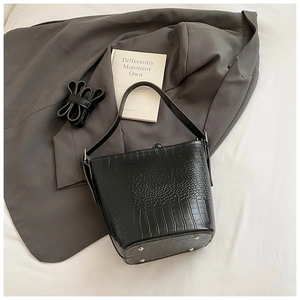 Detail of black crocodile pattern bucket bag with metal feet and detachable shoulder strap