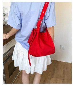 Side view of large red canvas shoulder bag with adjustable strap worn by a model