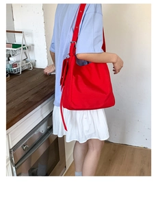 Detail of red canvas tote bag with wide shoulder strap and metal buckle on model