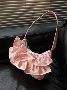 Pink crescent balletcore shoulder bag with ruffles and bow on black leather background