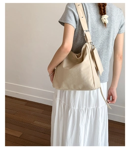 Detail of beige canvas shoulder bag featuring a wide adjustable strap and a small coin pouch