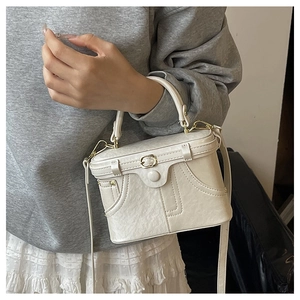 Close-up of cream retro box handbag featuring vintage stitching and gold metal buckle