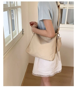 Close-up of beige canvas tote bag showing wide shoulder strap with silver metal buckle