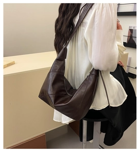 Detail of a vintage dark brown crescent shoulder bag worn by a model in a cafe setting