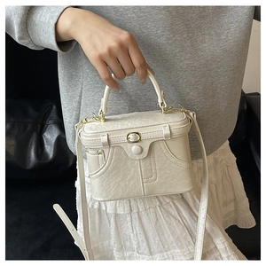 Detail of cream leather box bag featuring contrast stitching and golden clasp buckle