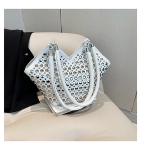 Vue détaillée du sac cabas blanc avec clous métalliques argentés sur un banc en cuir