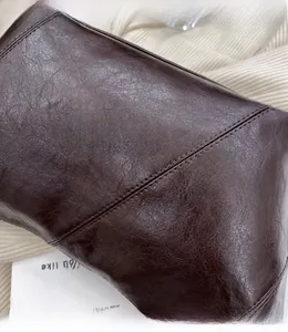 Close-up of deep brown oil-wax leather texture and fine stitching on a trendy dumpling bag