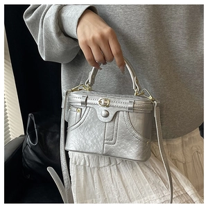 Detailed view of silver metallic box bag with golden buckle and decorative stitching