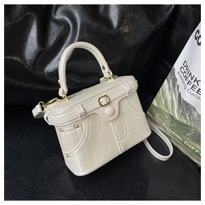 Close-up of white pleated leather bag with denim pocket design and gold rivets
