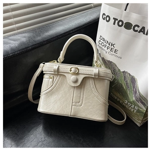 Close-up of beige box bag with denim pocket stitching and hardware on leather background