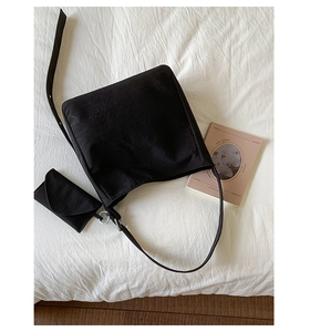 Top view of black canvas shoulder bag with small pouch on white fabric background
