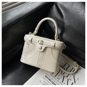 Detail of a creamy white structured handbag with gold hardware on a dark leather surface