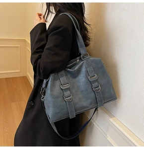 Blue high-capacity textured leather tote bag worn on shoulder by female model in elegant room