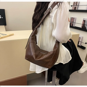 Detail of dark brown leather crescent bag showing adjustable strap with metal eyelets