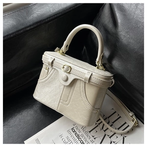 Detailed view of a vintage cream box bag with buckle accents on a leather background