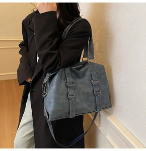 Close-up of a large blue washed tote bag with vintage metal buckles on a black coat