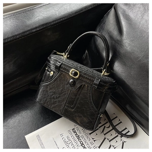 Detailed close-up of a vintage black box bag with a golden buckle on a leather sofa
