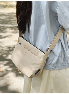 Détail du sac bandoulière en nylon crème montrant le tissu résistant et le logo côté
