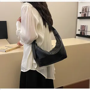 Detail of minimalist black matte leather hobo bag worn by model with wide shoulder strap