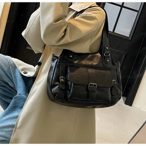 Detail of a black leather tote bag featuring a front pocket and metallic buckle detail