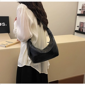 Detail of a minimalist black leather hobo bag worn over the shoulder with wide strap