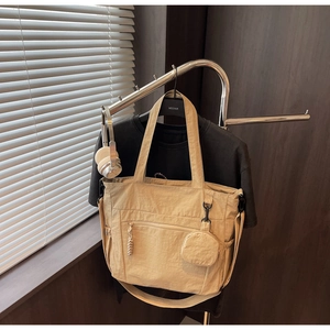Detail view of beige nylon tote bag showing front zipper pocket and round mini hanging pouch