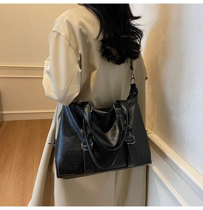 Detailed view of the large black leather tote bag with crinkle texture on a beige coat