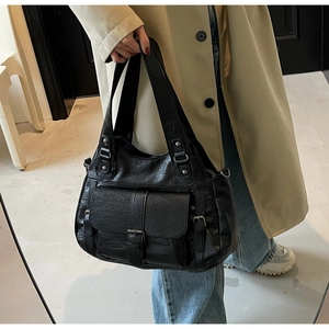 Detail of vintage black faux leather tote with metallic buckles on a model in trench coat